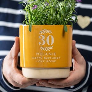 May include: Yellow ceramic planter with a white inscription that reads "30 Melanie Happy Birthday Love Rosie".