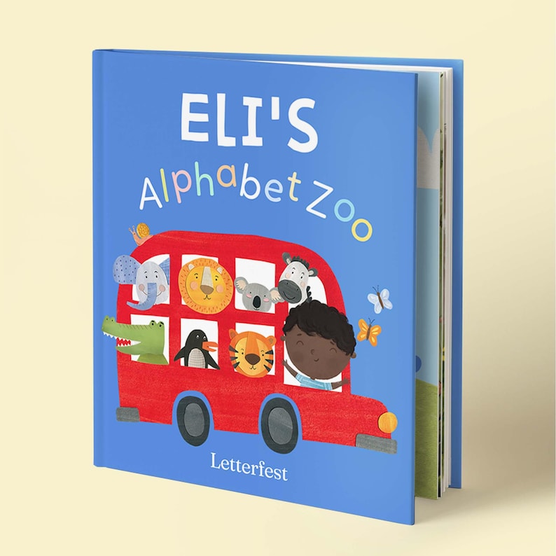May include: A blue hardcover children's book titled Eli's Alphabet Zoo. The cover features a red bus filled with illustrated animals including an elephant, lion, koala, zebra, crocodile, penguin, and tiger, with a child driving and butterflies.