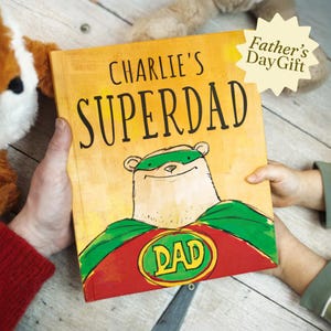 May include: A children's book titled "Charlie's Superdad" with a cartoon bear superhero on the cover. The book has a yellow background with red and green accents. The words "Father's Day Gift" are also visible.