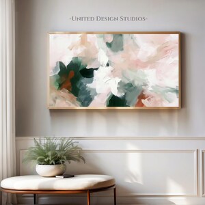 May include: Abstract painting with a gold frame. The painting features shades of pink, green, and white. The painting is hanging on a white wall.
