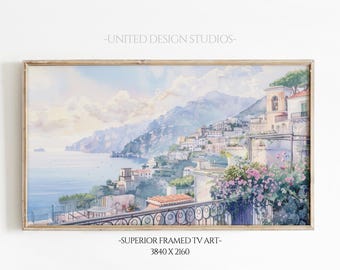 May include: A watercolor painting of a coastal town with colorful buildings on a hillside overlooking a blue ocean. The painting is framed in a light wood frame. The text "UNITED DESIGN STUDIOS" and "SUPERIOR FRAMED TV ART - 3840 X 2160" is printed below the image.