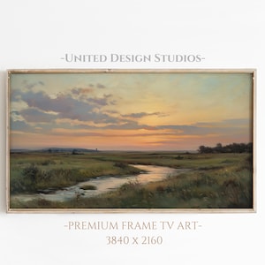 May include: A framed landscape painting depicting a river winding through a grassy field at sunset. The sky is a soft blend of pink, orange, and blue with fluffy clouds. The painting is in a light wood frame.