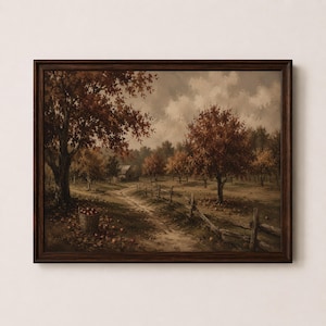 May include: A framed landscape painting depicting an orchard with autumn-colored trees, a dirt path, a wooden fence, and a small building in the distance. A wooden basket filled with red apples sits on the ground near a large tree in the foreground.