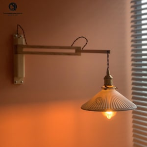 May include: A wall-mounted wooden swing arm lamp with a ribbed glass shade. The lamp has a brass-coloured bulb holder and a visible filament bulb, emitting a warm glow. The wooden arm is attached to the wall with a rectangular wooden base. The lamp is a vintage style.