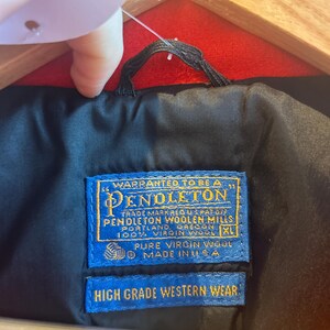 May include: Close-up of a black jacket lining with a blue Pendleton label. The label reads "Warranted to be a Pendleton" and "High Grade Western Wear." The jacket is made of 100% virgin wool and is a size XL.