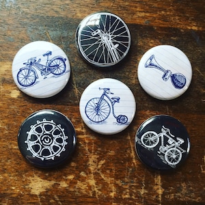 May include: Six round, white and black buttons with blue ink drawings of bicycles and bicycle parts. The buttons feature a bicycle horn, a bicycle wheel, a penny-farthing bicycle, a bicycle with a basket, a bicycle with a bell, and a bicycle with a spoke wheel.