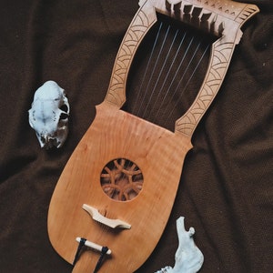 May include: A wooden lyre with a carved design and a sound hole. The lyre is on a brown fabric background with two white animal bones.