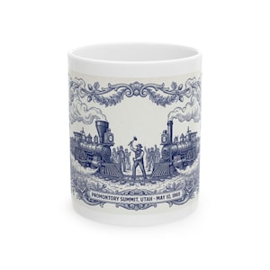 May include: White ceramic mug featuring a blue and white illustration of two trains facing each other with a man in the middle. The text "PROMONTORY SUMMIT, UTAH - MAY 10, 1869" is printed at the bottom.