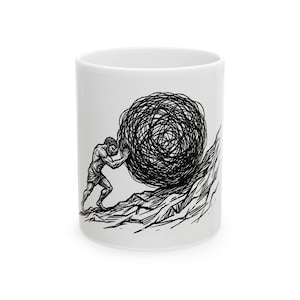 May include: White ceramic mug featuring a black and white illustration of a person pushing a large, tangled ball up a mountain. The design is a stylized depiction of the Greek myth of Sisyphus. The mug has a standard cylindrical shape.