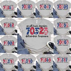 May include: A collection of gray t-shirts with the text "small town freedom" and various zip codes in red, white, and blue. Each shirt features a different Louisiana town name. The shirts are displayed on a flat surface.