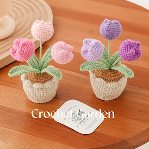 May include: Two crocheted flower arrangements with pink and purple tulips in brown pots. The pots are sitting on a wooden table. The card reads "Hand made with Love Crochet Garden by Layla".