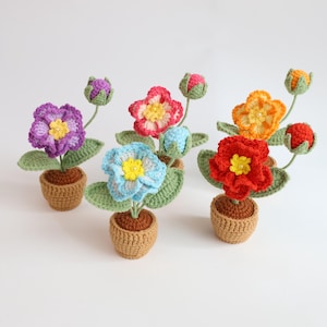 May include: A collection of handmade crochet flowers in small brown pots. The flowers are in various colors, including purple, pink, blue, orange, and red, each with a yellow center. Green leaves and buds accompany the flowers, creating a vibrant display.
