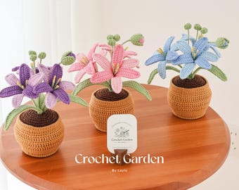 May include: Three crocheted lily flower arrangements in pots. The lilies are pink, purple, and blue. The pots are a light brown color. The flowers are arranged on a wooden table. The text "Crochet Garden by Layla" is on a small sign in front of the flowers.