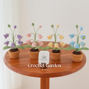 May include: Four crocheted flower arrangements in pots. The flowers are purple, pink, yellow, and blue. The pots are brown and the flowers are in a bell shape. The flowers are arranged on a wooden table with a sign that reads "Crochet Garden by Layla".