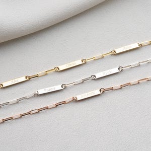 May include: Three personalised bar necklaces in gold, silver, and rose gold. Each necklace features a rectangular bar with an engraved name: Alex, Olivia, Rick, Poppy, Frank, and Adam. The chains are delicate and the background is a soft white.