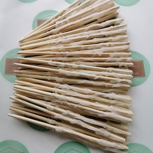 May include: A close-up of a pile of wooden wands with clear glue applied to them. The wands are all about 20 cm long and are made of natural wood.