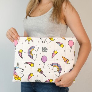 Peut inclure: Une trousse de maquillage matelassée blanche avec un motif de licorne, d'arc-en-ciel, d'étoile et de couronne rose, jaune et bleu.
