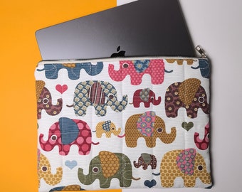 May include: A white laptop sleeve with a quilted design featuring colorful patchwork elephants. The sleeve has a zipper closure and is designed to protect a laptop.