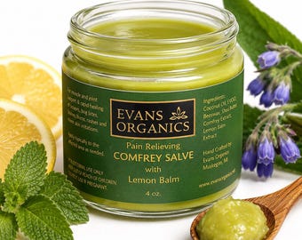 May include: A clear glass jar of green comfrey salve with a dark green label reading Evans Organics Pain Relieving Comfrey Salve with Lemon Balm 4 oz. The jar is surrounded by lemon slices, mint leaves, and purple flowers, with a wooden spoon of salve.
