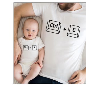 May include: A white t-shirt with the text "Ctrl + C" on the front. A baby is wearing a white onesie with the text "Ctrl + V" on the front.