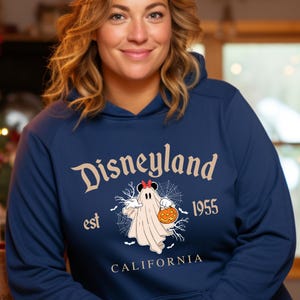 Puede incluir: Sudadera con capucha azul marino con "Disneyland" en una fuente vintage. El dise&ntilde;o incluye un fantasma con un lazo de Minnie Mouse y una calabaza, con "est 1955 CALIFORNIA" debajo. Una sudadera con tem&aacute;tica de Halloween.