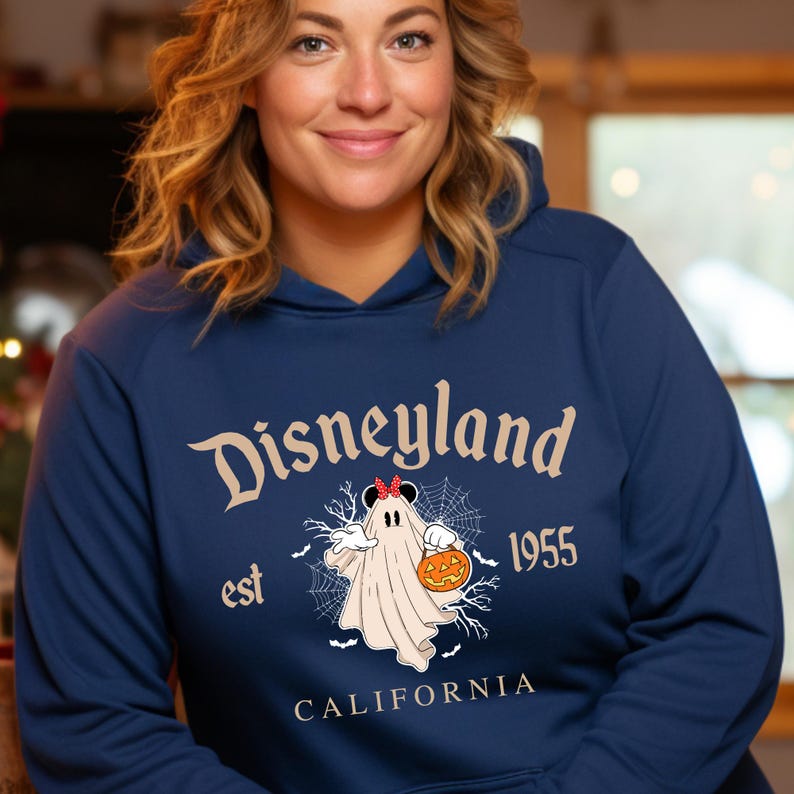 Puede incluir: Sudadera con capucha azul marino con "Disneyland" en una fuente vintage. El dise&ntilde;o incluye un fantasma con un lazo de Minnie Mouse y una calabaza, con "est 1955 CALIFORNIA" debajo. Una sudadera con tem&aacute;tica de Halloween.