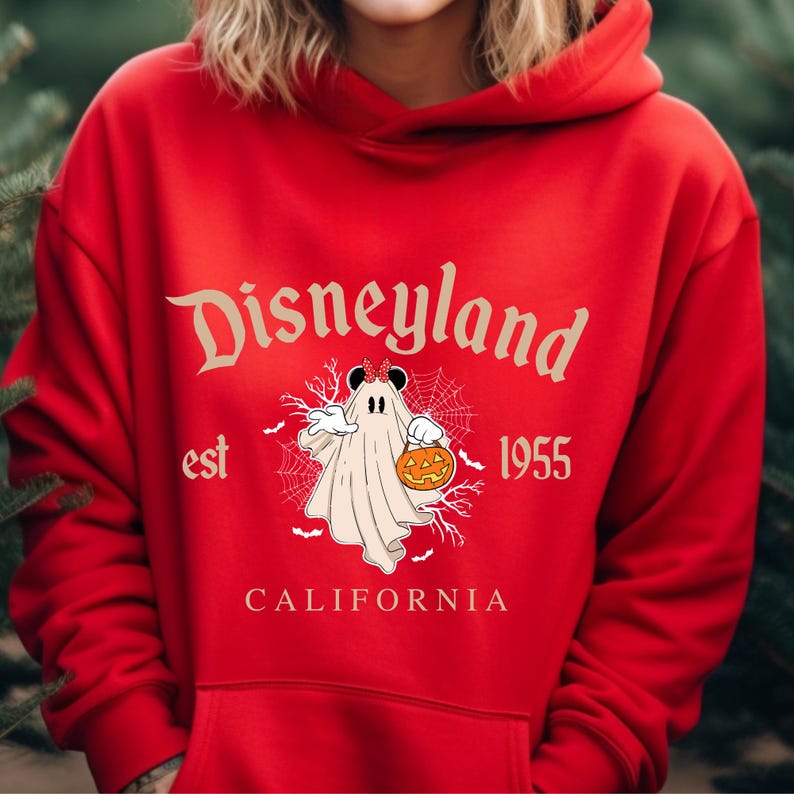 Puede incluir: Una sudadera con capucha roja con el logotipo de Disneyland y un gr&aacute;fico de Halloween. El gr&aacute;fico muestra un fantasma disfrazado de Mickey Mouse sosteniendo una calabaza, con el texto "Disneyland est 1955 California".