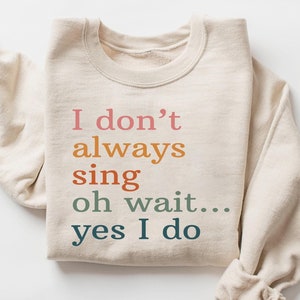 May include: A beige sweatshirt with the text "I don't always sing oh wait... yes I do" printed in colorful letters.