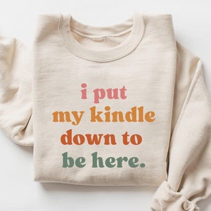 May include: A beige sweatshirt with the text "i put my kindle down to be here." printed in rainbow colors.