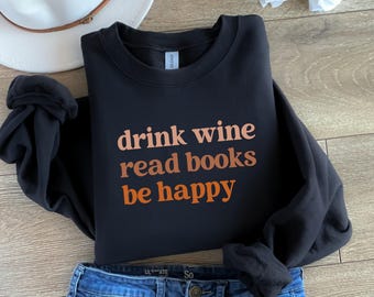 May include: Black sweatshirt with the text "drink wine read books be happy" in orange and brown lettering.