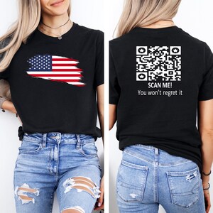 May include: Black t-shirt with a distressed American flag design on the front and a QR code with the text "SCAN ME! You won't regret it" on the back.