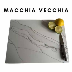 May include: White marble cutting board with gray veining. The board has a knife and three limes on it. The text "MACCHIA VECCHIA" is at the top of the image.