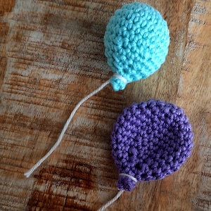 Puede incluir: Dos globos de crochet, uno azul claro y otro morado, con cuerdas blancas atadas.