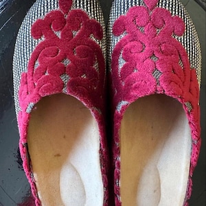 Peut inclure: Une paire de pantoufles noires et argentées avec un motif floral en velours rouge. Les pantoufles ont une doublure douce et confortable.