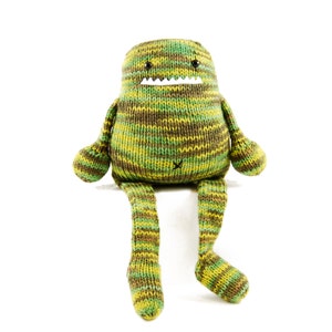 Pode incluir: Um brinquedo de monstro de malha listrada verde e marrom com um sorriso de dentes e olhos pretos. O monstro est&aacute; sentado com as pernas esticadas.
