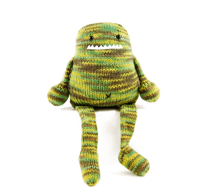 Pode incluir: Um brinquedo de monstro de malha listrada verde e marrom com um sorriso de dentes e olhos pretos. O monstro est&aacute; sentado com as pernas esticadas.