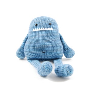 Pode incluir: Um monstro de pel&uacute;cia azul de malha com uma boca de feltro branco e olhos pretos. O monstro tem bra&ccedil;os e pernas longos.
