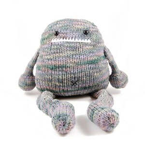 Pode incluir: Um brinquedo de monstro de malha cinza, rosa e verde com olhos pretos e uma boca branca costurada. O monstro tem dois bra&ccedil;os longos e duas pernas longas.