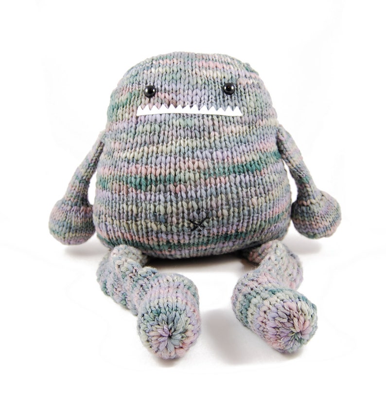 Pode incluir: Um brinquedo de monstro de malha cinza, rosa e verde com olhos pretos e uma boca branca costurada. O monstro tem dois bra&ccedil;os longos e duas pernas longas.