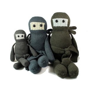 May include: Three knitted plush toys shaped like ninjas, one large, one medium, and one small. The ninjas are wearing black, dark gray, and light gray masks. The large ninja is wearing a dark green outfit with a white sash. The medium ninja is wearing a dark gray outfit. The small ninja is wearing a light gray outfit.