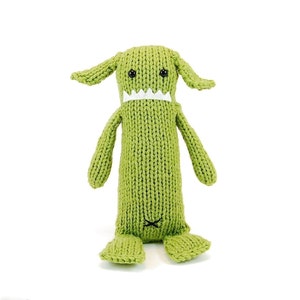 Op de afbeelding: Groen gebreid monster speelgoed met witte tanden en zwarte ogen. Het speelgoed heeft lange armen en benen en een kleine staart.