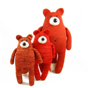 May include: Three knitted plush toys shaped like foxes in different sizes. The largest fox is red with black eyes and a white nose. The middle fox is red with black eyes and a white nose. The smallest fox is red with black eyes and a white nose.