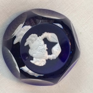 Pu&ograve; includere: Un cabochon in vetro blu scuro sfaccettato con un rilievo bianco di un granchio. Il granchio &egrave; centrato su un cerchio blu scuro. Il cabochon ha una forma ottagonale sfaccettata.