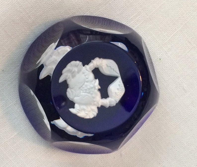 Pu&ograve; includere: Un cabochon in vetro blu scuro sfaccettato con un rilievo bianco di un granchio. Il granchio &egrave; centrato su un cerchio blu scuro. Il cabochon ha una forma ottagonale sfaccettata.