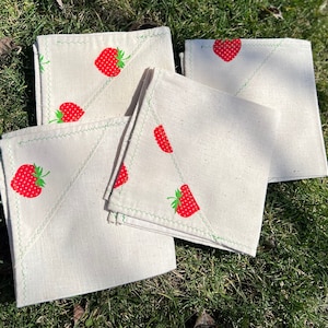 May include: Set of four white cotton tea towels with a green stitched border and a red strawberry print.
