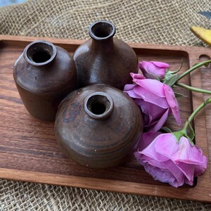 May include: Three small brown ceramic vases on a wooden tray with pink flowers.