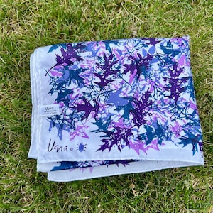 May include: A white square scarf featuring a repeating pattern of oak leaves in shades of purple, violet, and blue. The fabric includes a small white tag reading "Usna 100% polyester Made in Japan" and a logo with the text "Usna" and a small blue beetle icon.