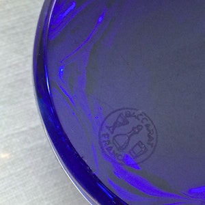 Pu&ograve; includere: Primo piano di un oggetto in vetro blu cobalto di forma circolare. Il vetro ha una finitura lucida e un motivo a spirale. &Egrave; visibile un timbro circolare con la scritta "BACCARAT FRANCE".
