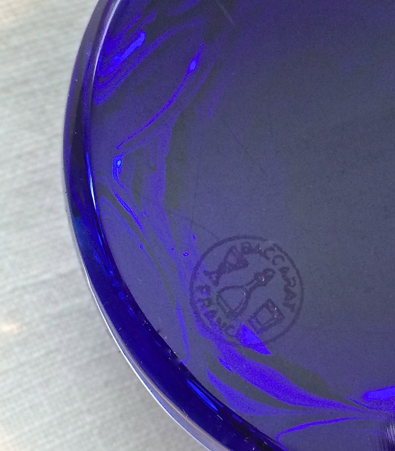 Pu&ograve; includere: Primo piano di un oggetto in vetro blu cobalto di forma circolare. Il vetro ha una finitura lucida e un motivo a spirale. &Egrave; visibile un timbro circolare con la scritta "BACCARAT FRANCE".