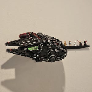 Puede incluir: Una nave espacial Lego Millennium Falcon negra y roja con una cabina verde, expuesta en un estante de pared con un grupo de personajes de Lego Star Wars.
